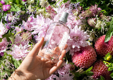 holding cherry blossom eau de toilette in front of garden and flowers